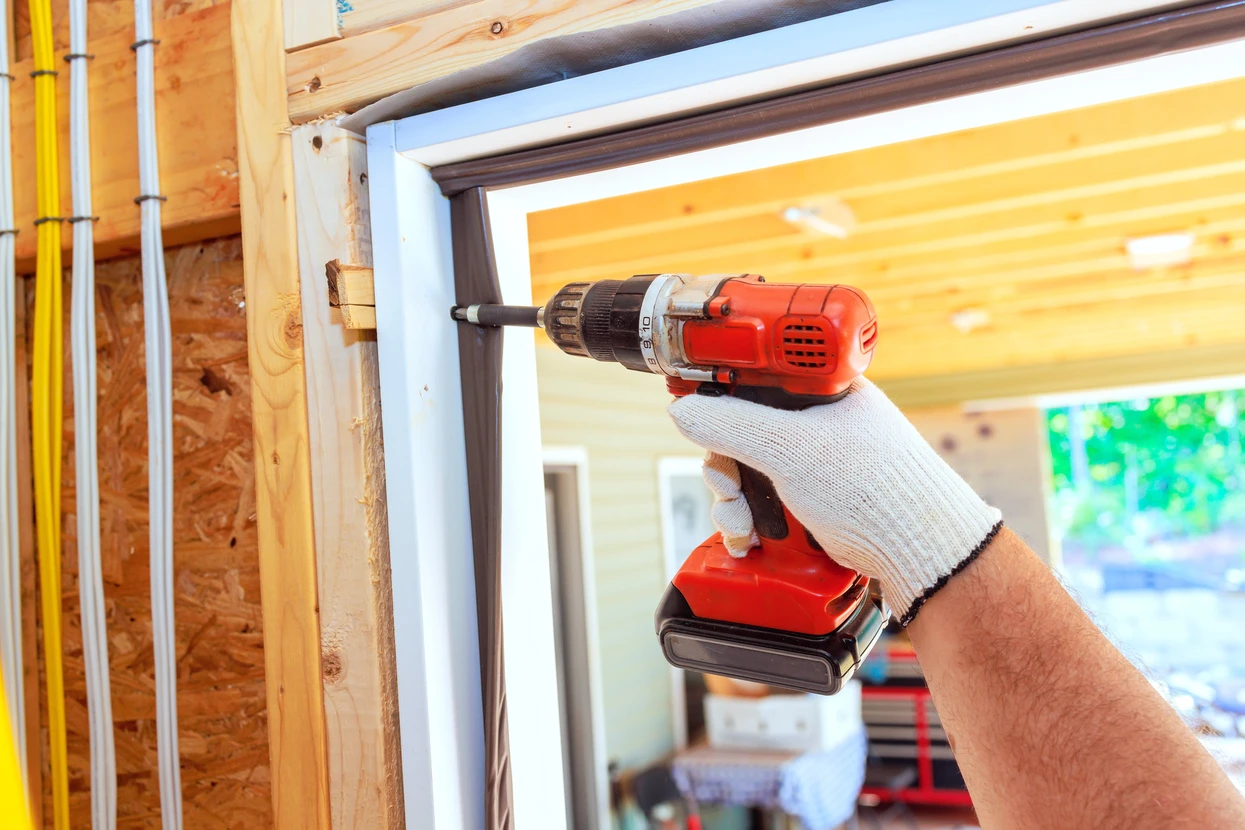Chantier de construction intérieur avec ouvrier utilisant une perceuse-visseuse sans fil rouge pour fixer une fenêtre PVC blanc