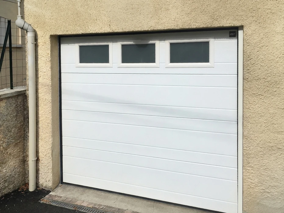 Porte de garage sectionnelle blanche avec rainures horizontales, équipée de trois hublots rectangulaires fumés en partie haute
