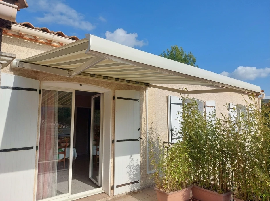 Store banne à toile rayée beige et taupe, entièrement déployée sur une terrasse extérieure de maison provençale