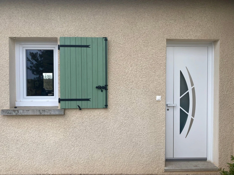 Entrée de maison contemporaine, façade blanche, porte d'entrée noire avec vitrage décoratif artistique aux tons chauds (rouge, orange, ocre)